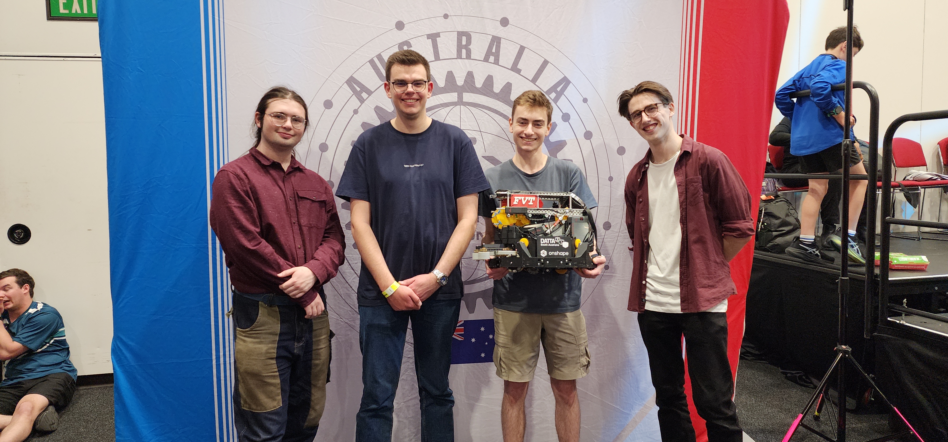 Picture of the team at the 2025 Australian National Championships, standing in front of the Australian VEX National Championship banner with their robot.