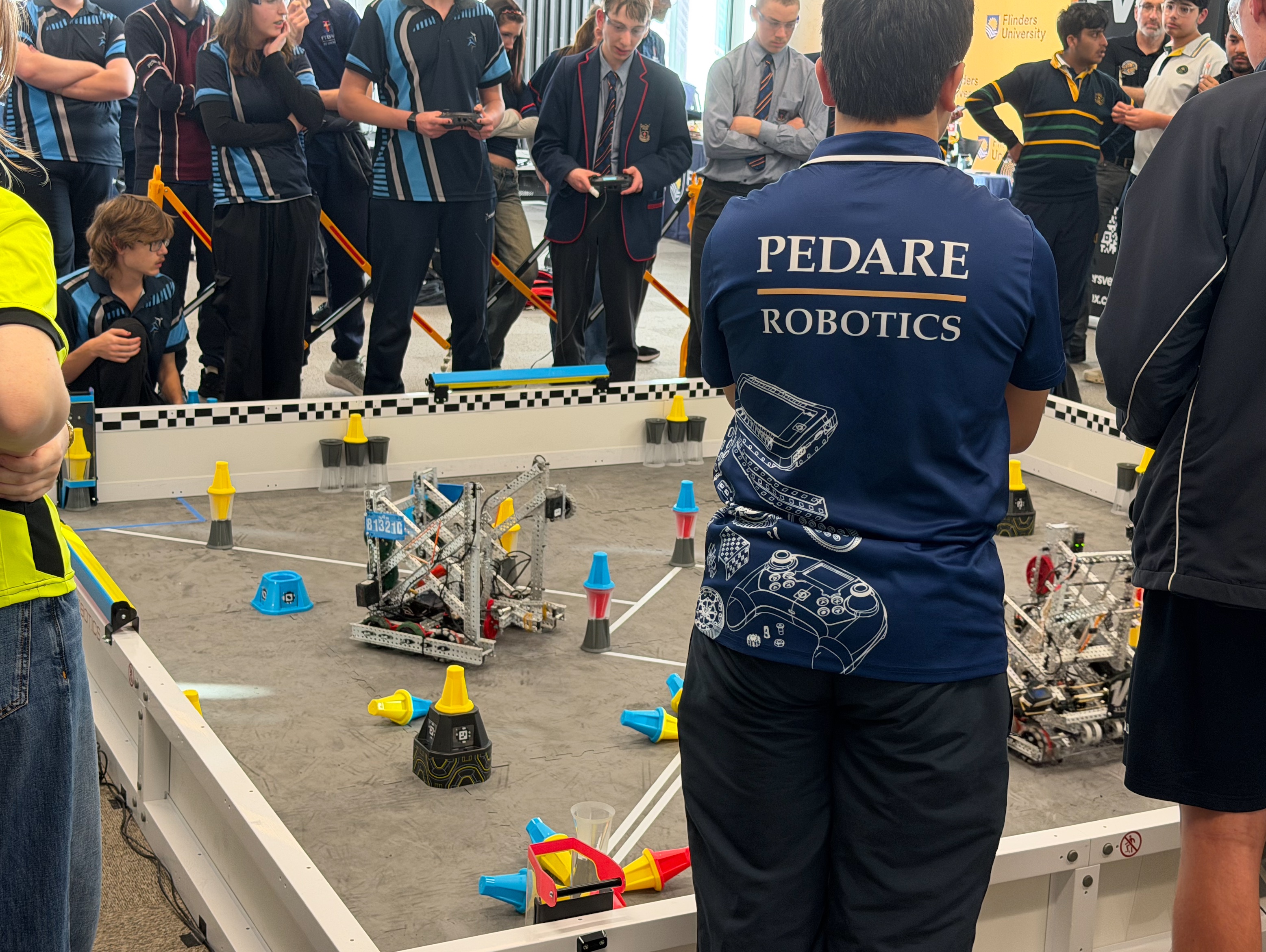 Image of an audience surronding a VEX Robotics Competition field, with multiple VEX robots and two teams competing for the top score.