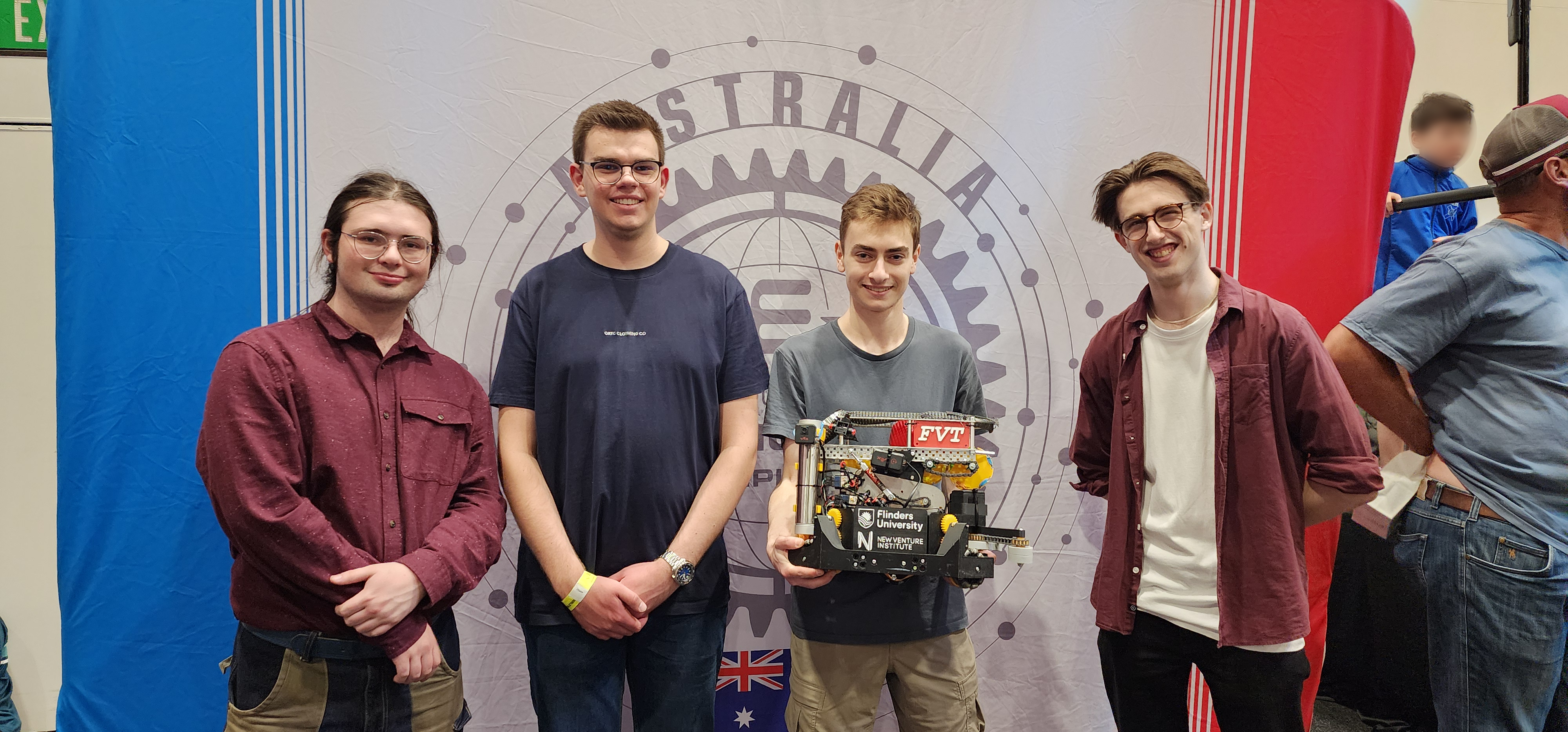 Four club members cheering next to and looking at a VEX Robotics field.
